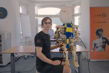 Mann sitzt mit einem Roboter an einem Tisch
